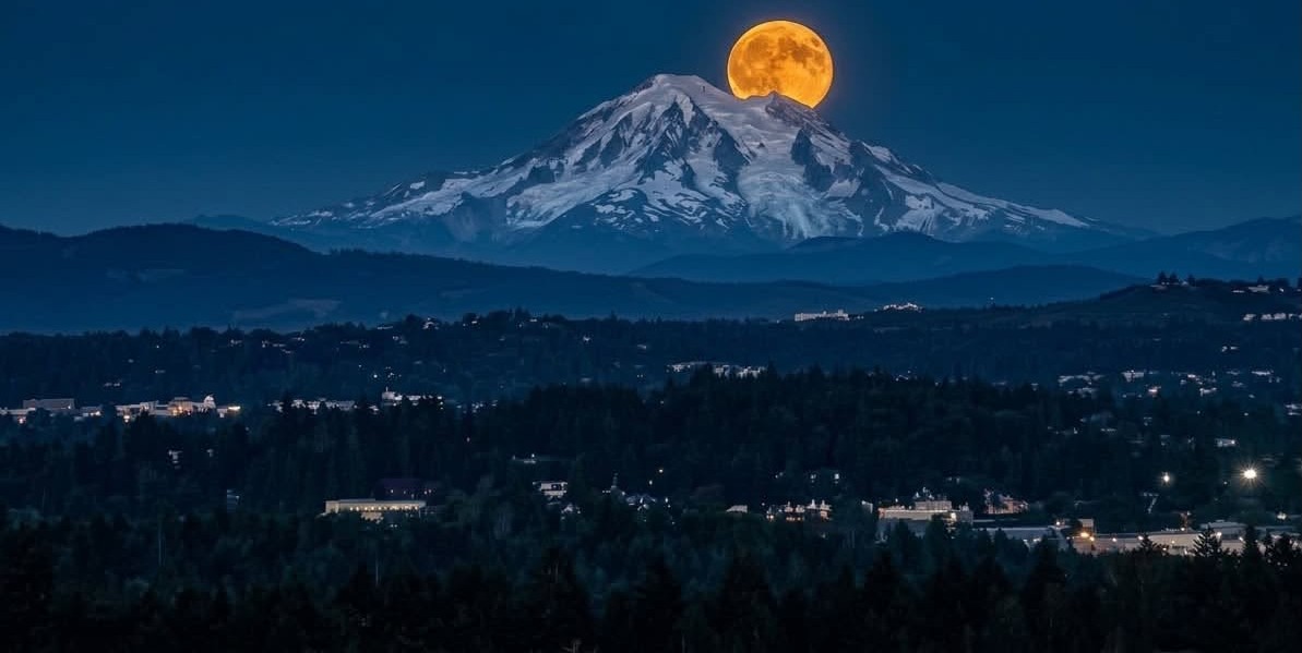 A full orange moon rising behind a snow-covered mountain peak at night